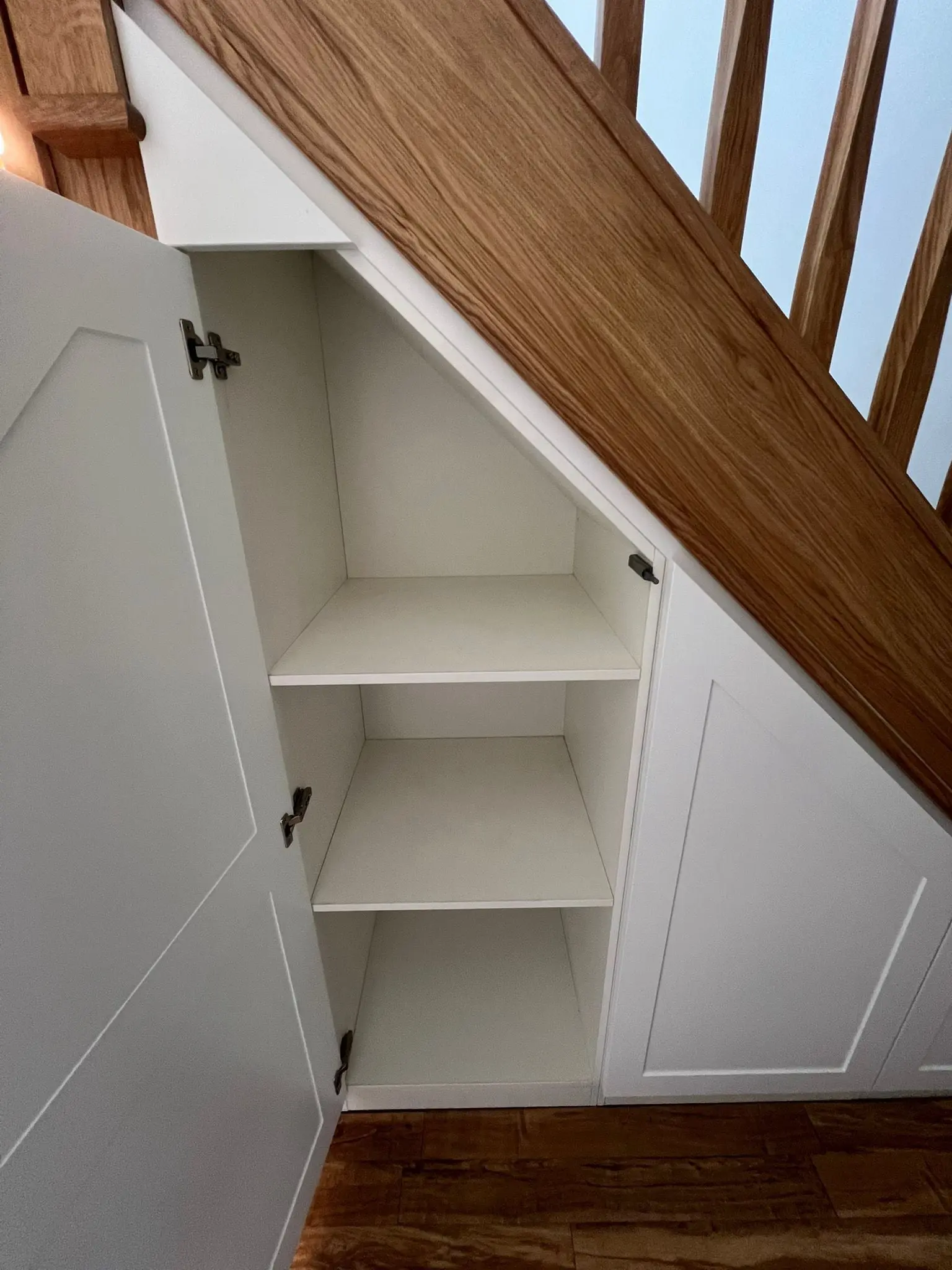 Under stairs storage solution for a tight staircase with angled drawers and doors
